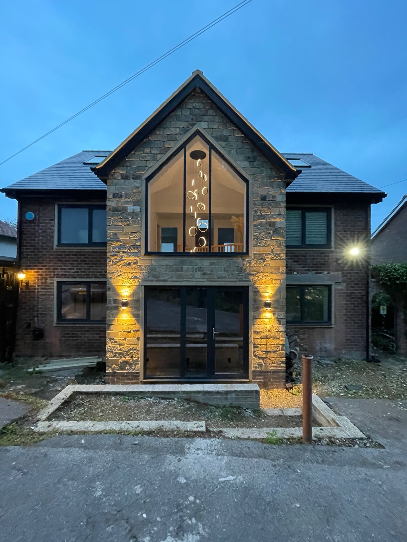 Completed stone-fronted house at dusk with a feature gable window and warm uplighting