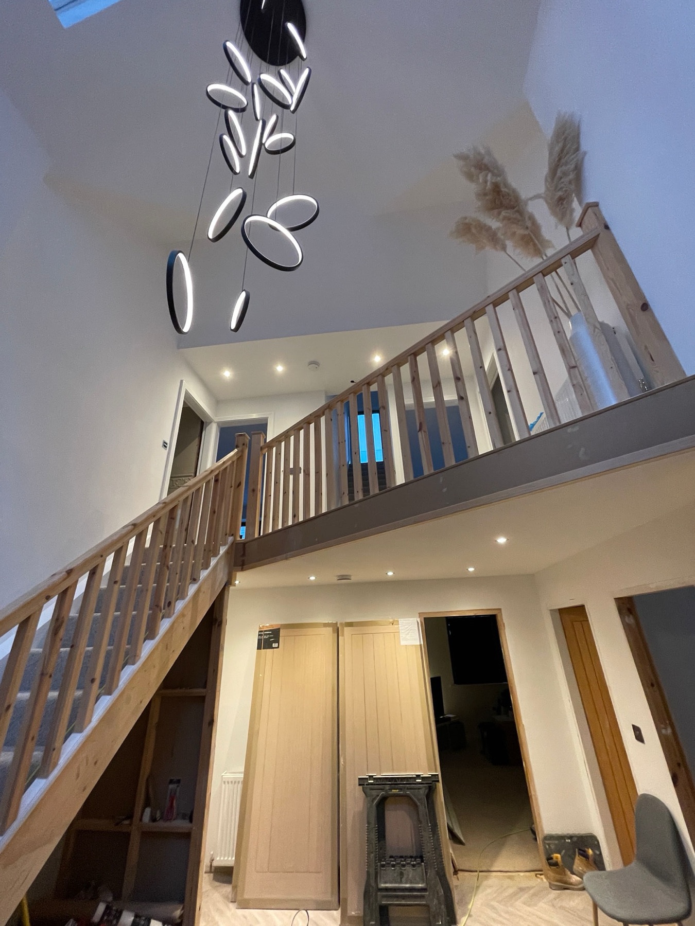 Double-height interior atrium with timber staircase and a cluster of ring pendant lights