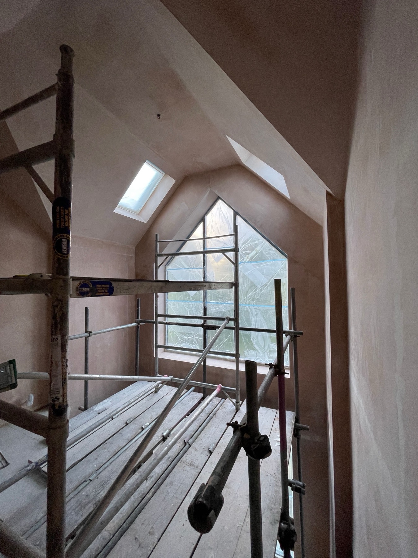 Vaulted loft conversion mid-renovation with fresh plaster, scaffolding and apex glazing